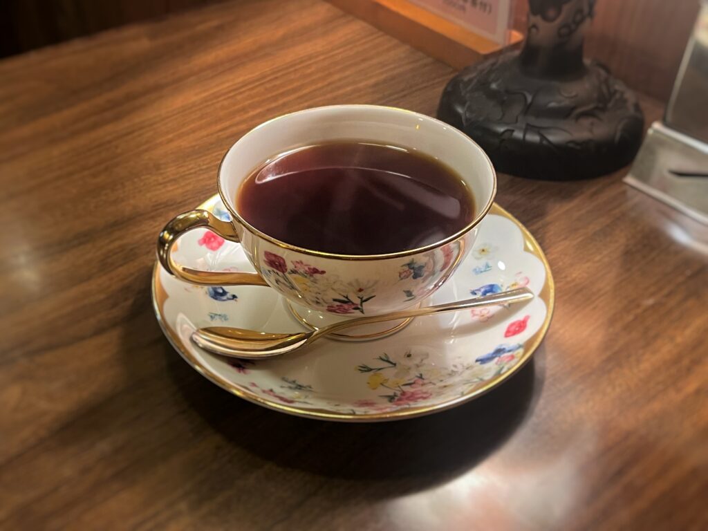 花柄のカップに注がれたブラックコーヒーが木製のテーブルの上に置かれている。